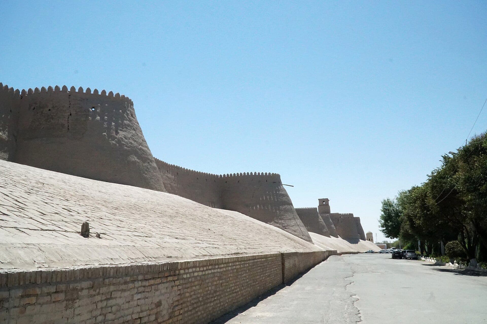 The clay walls of Itchan Kala in Khiva: sloping ramparts and rounded crenellated towers running beside a quiet road