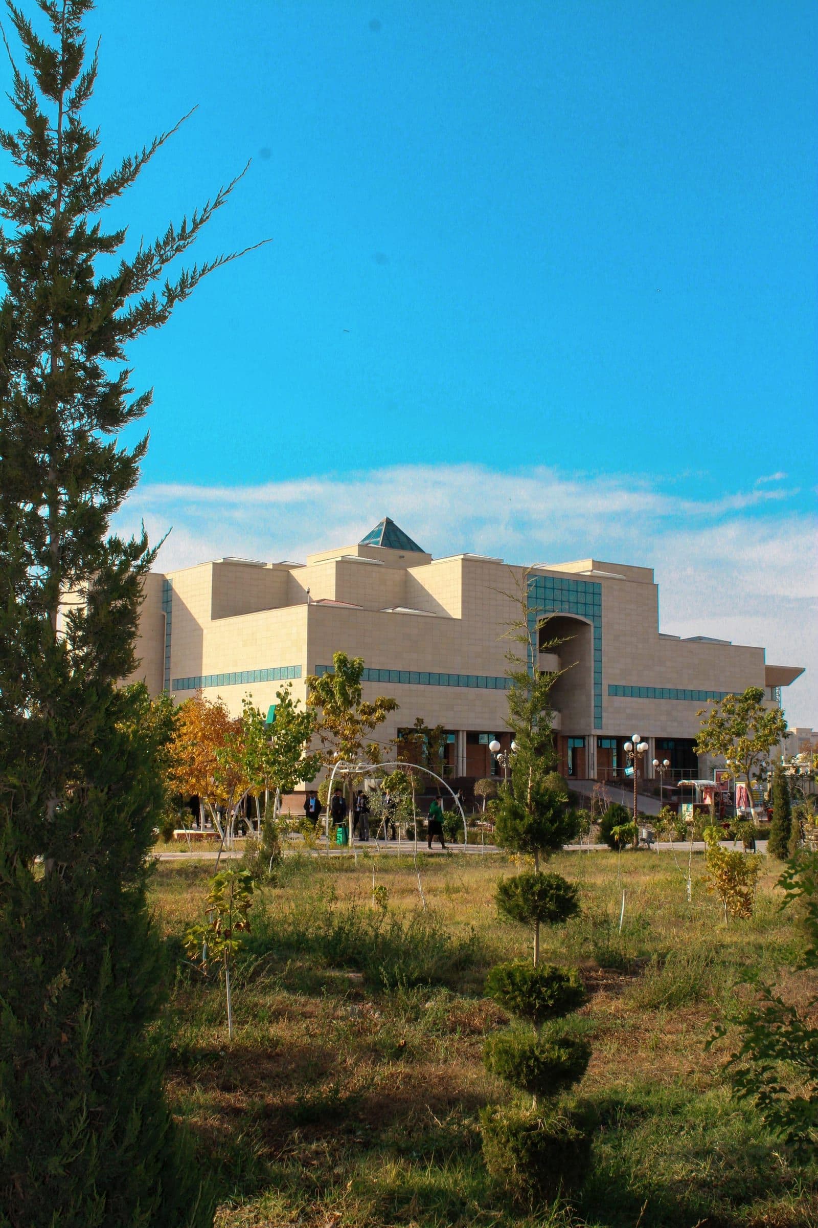 Savitsky Museum in Nukus: a pale stone building with turquoise bands, seen across a park of young trees