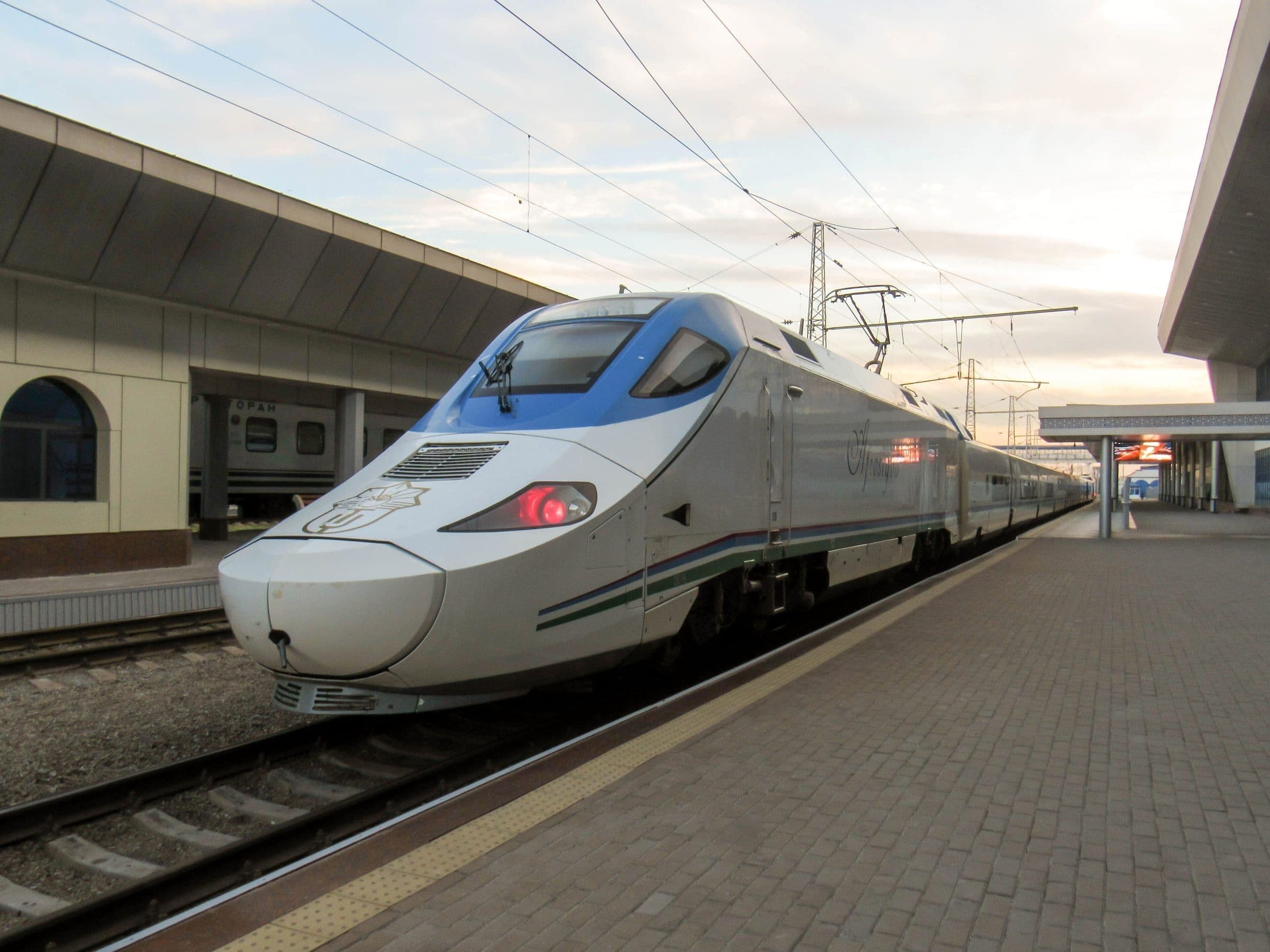 The white-and-blue Afrosiyob high-speed train at a station platform, stripes in the Uzbek flag's colours along its side