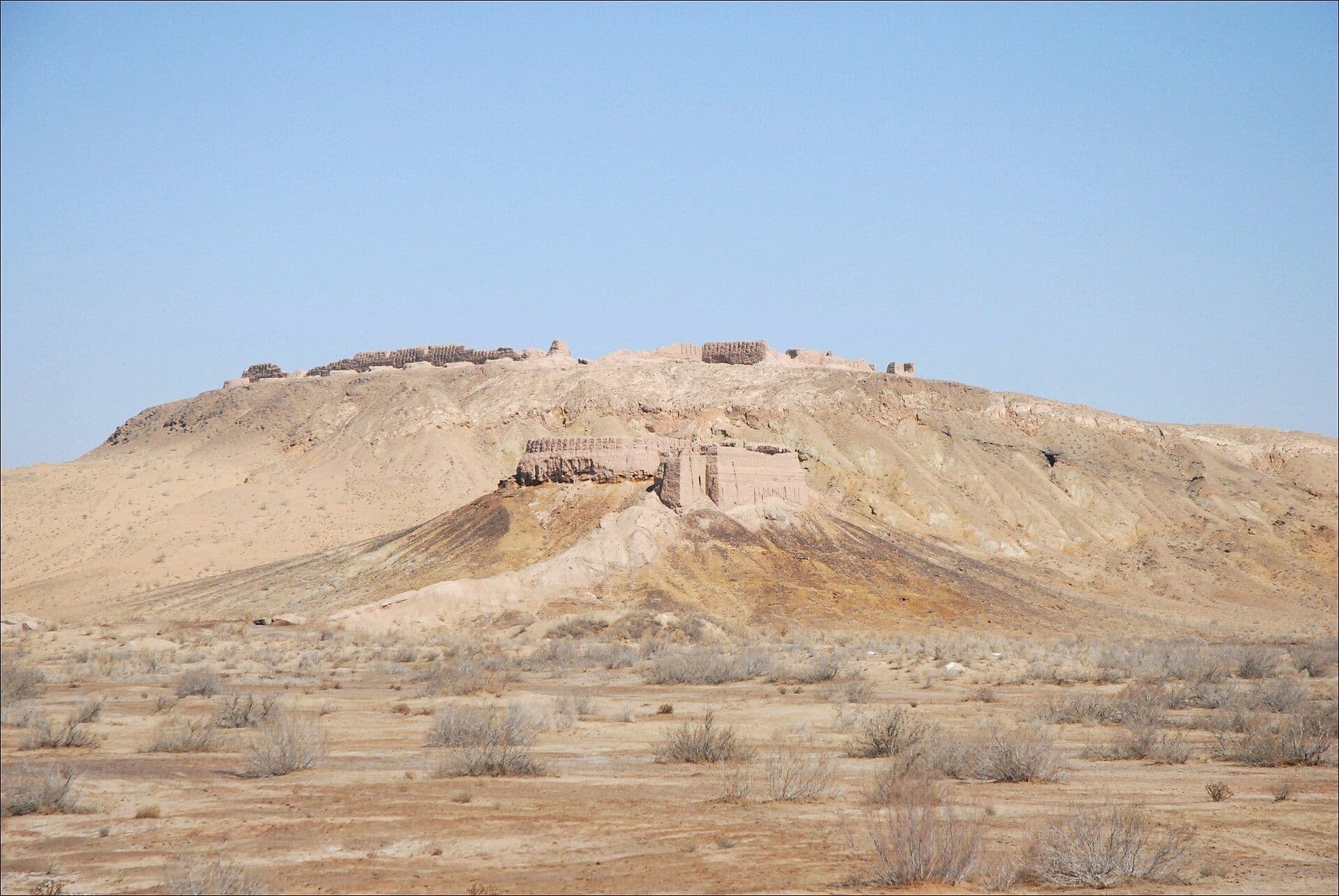 Mud-brick walls of Ayaz-Kala crowning a bare desert hill, with more ruined walls on the slope below