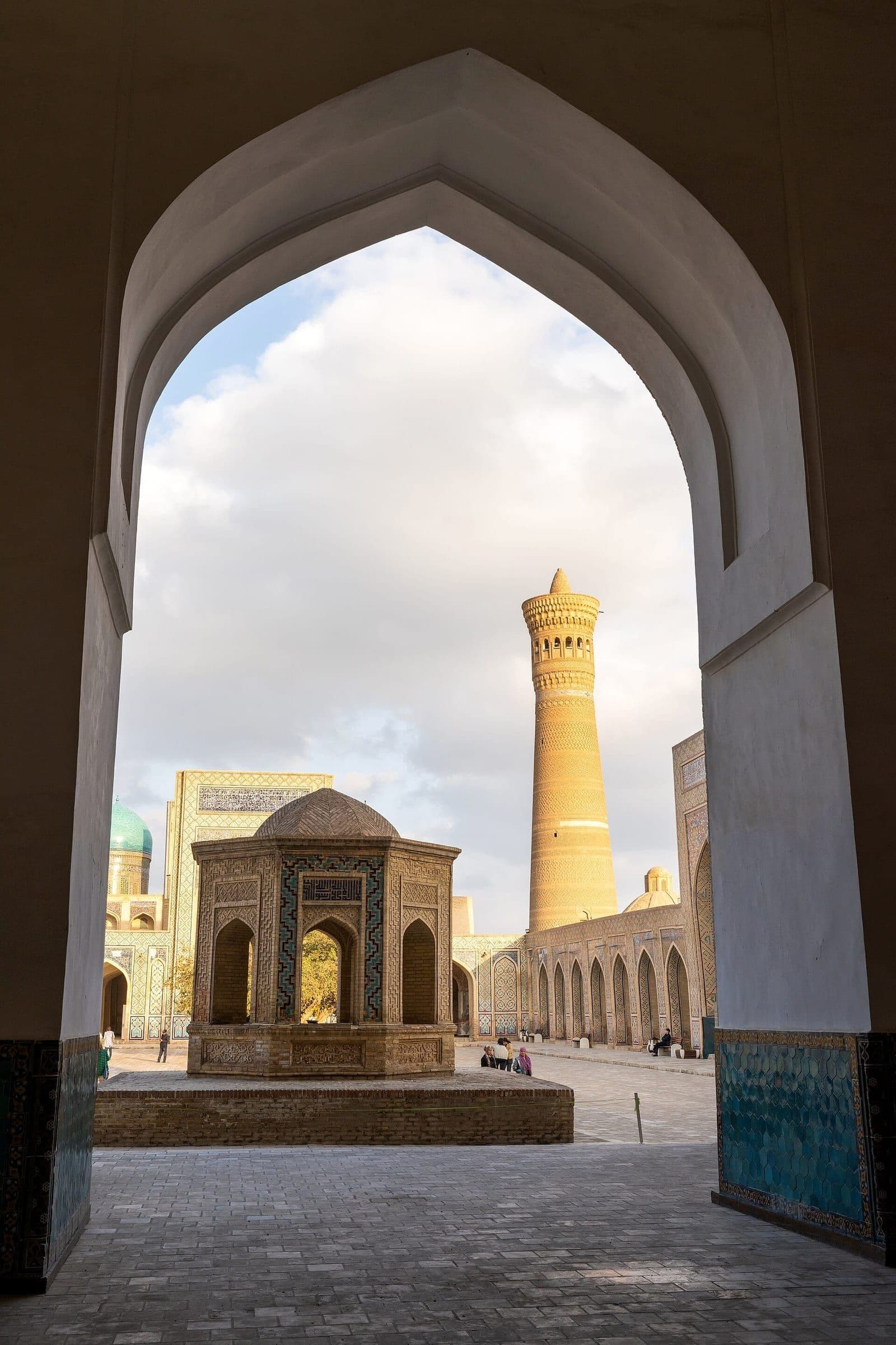 The Kalyan Minaret in Bukhara framed by a tall pointed arch, beyond a courtyard with a domed octagonal pavilion