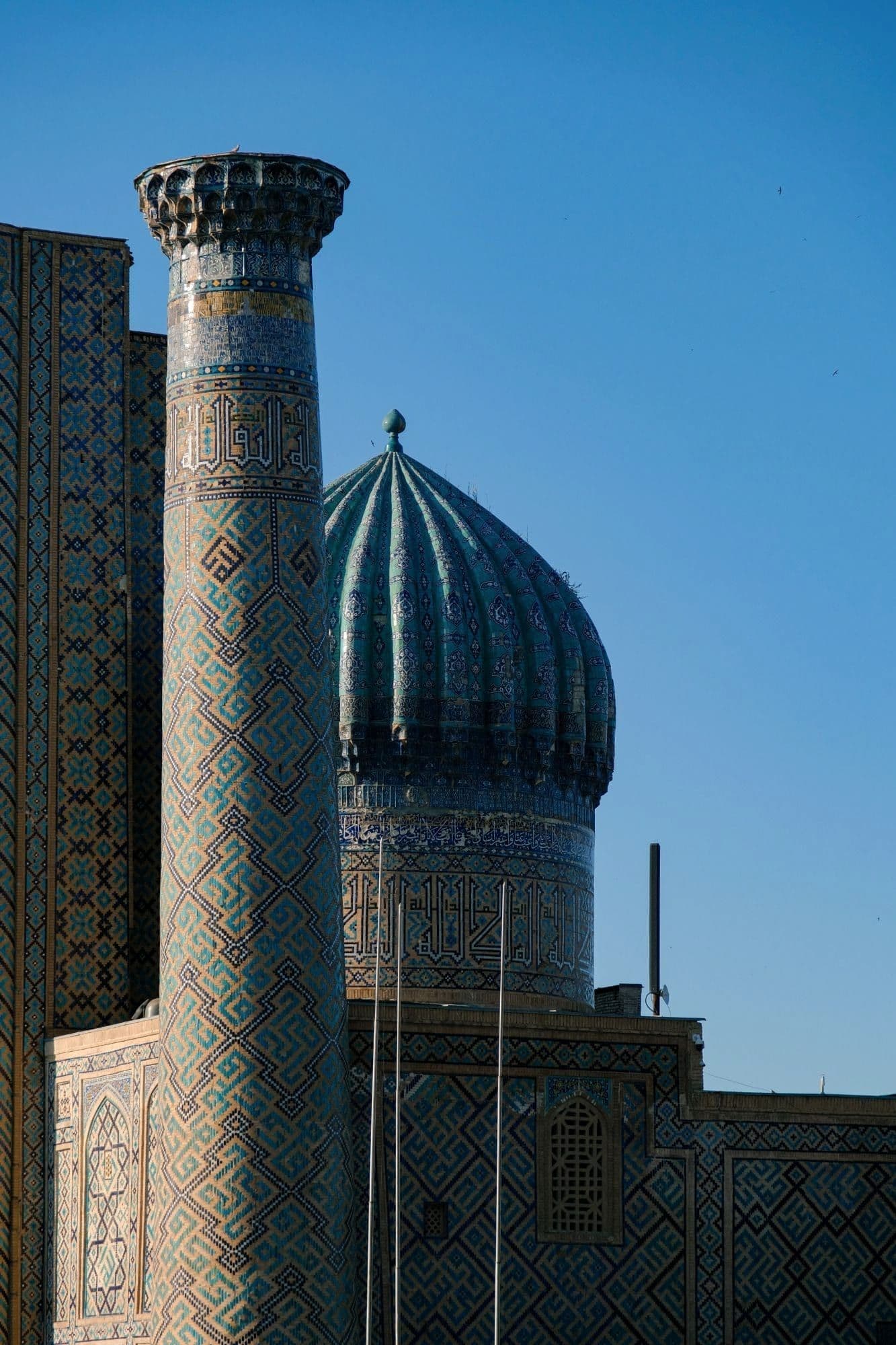 Sher-Dor madrasa on Registan, Samarkand: a tiled minaret and ribbed turquoise dome against a clear blue sky