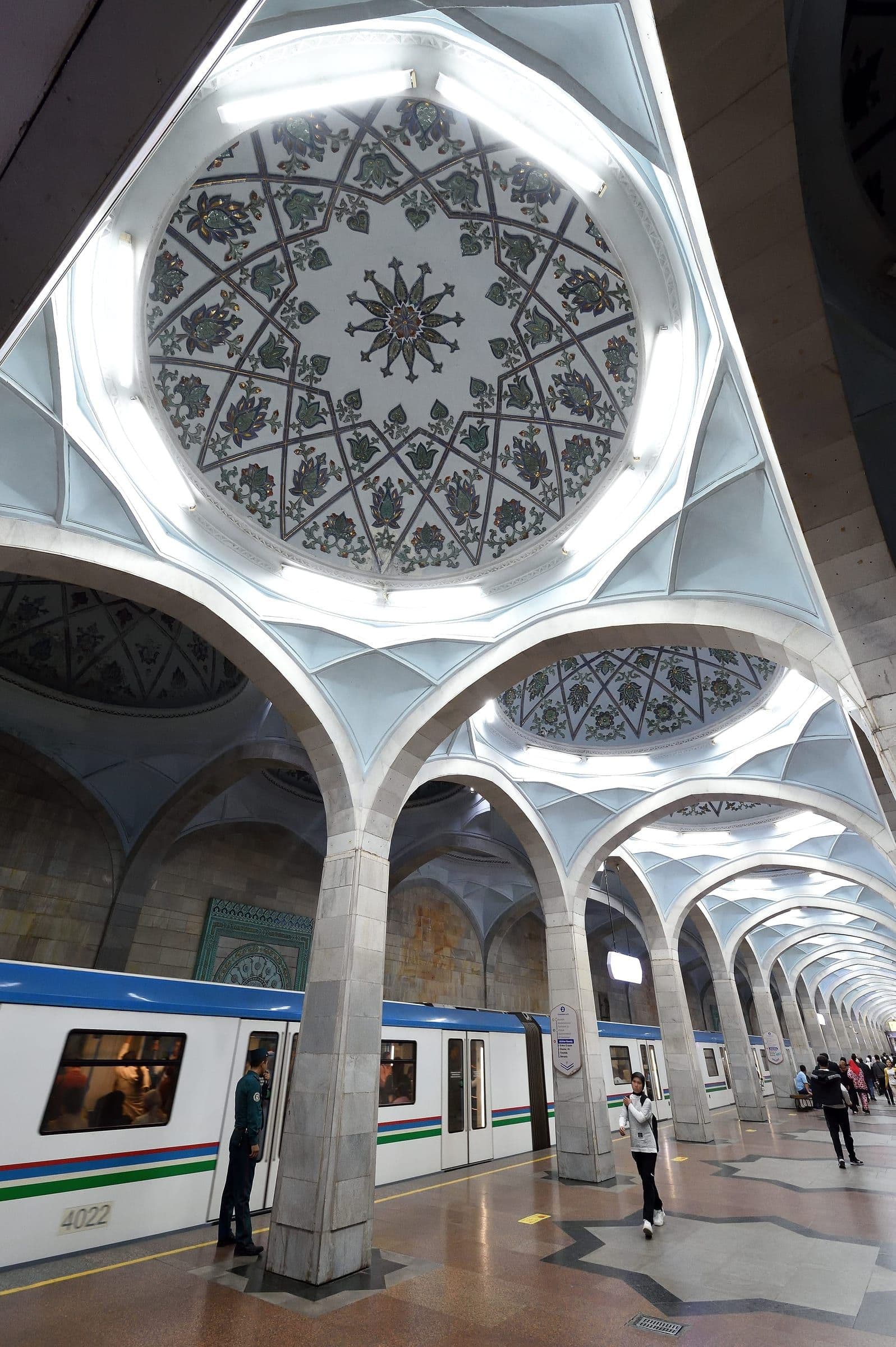 A Tashkent metro station: white arches and painted floral domes over the platform, with a train standing alongside